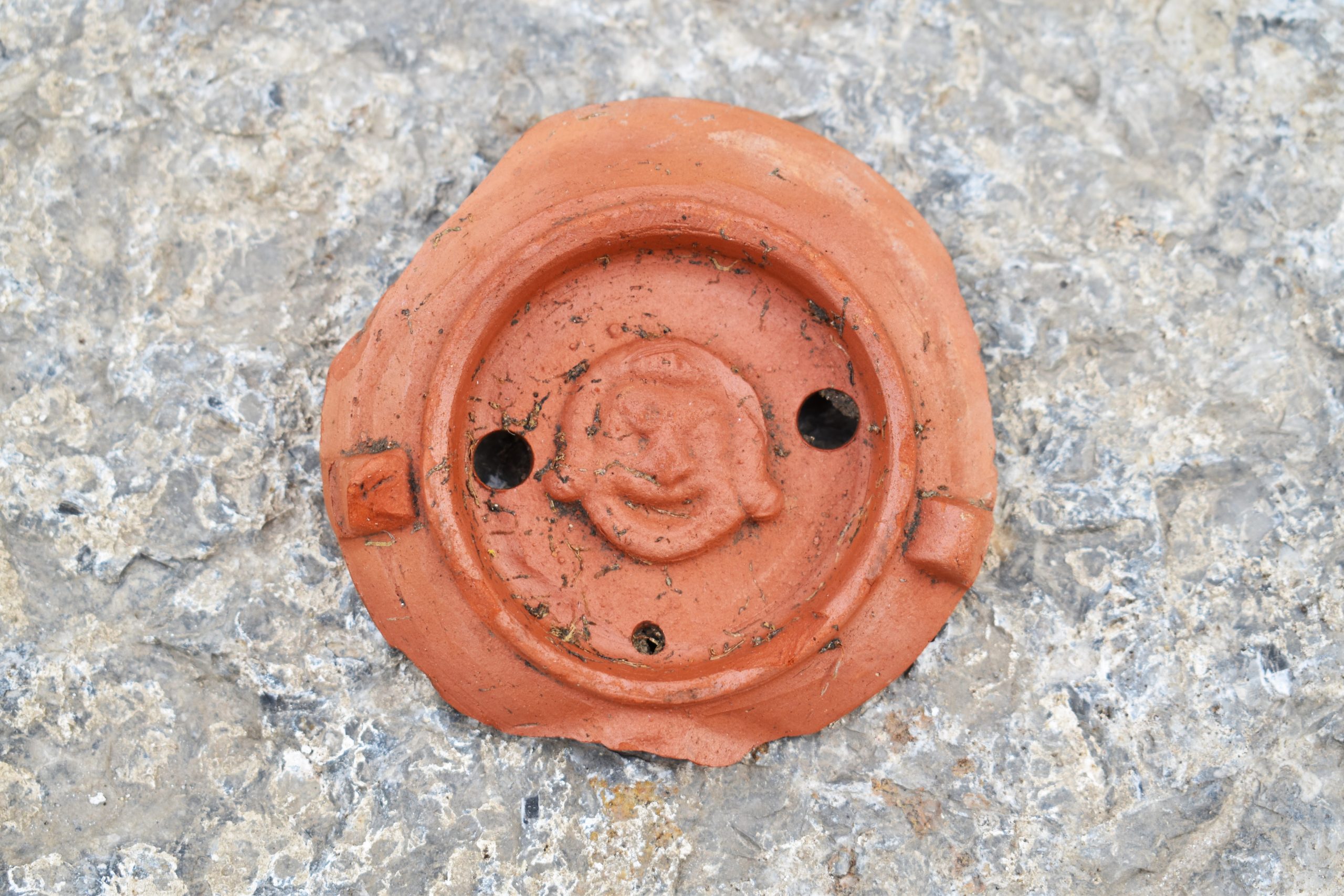 Rimska oljenka - svetilka z gledališko masko (velikost: d. 7,5; š. 7,5 cm), verjetno sodi v 2. stoletje. Našli smo jo v jami na področju ceste cardo A, v izkopnem polju ob Igriški ulici (foto: Tilen Kozamernik).